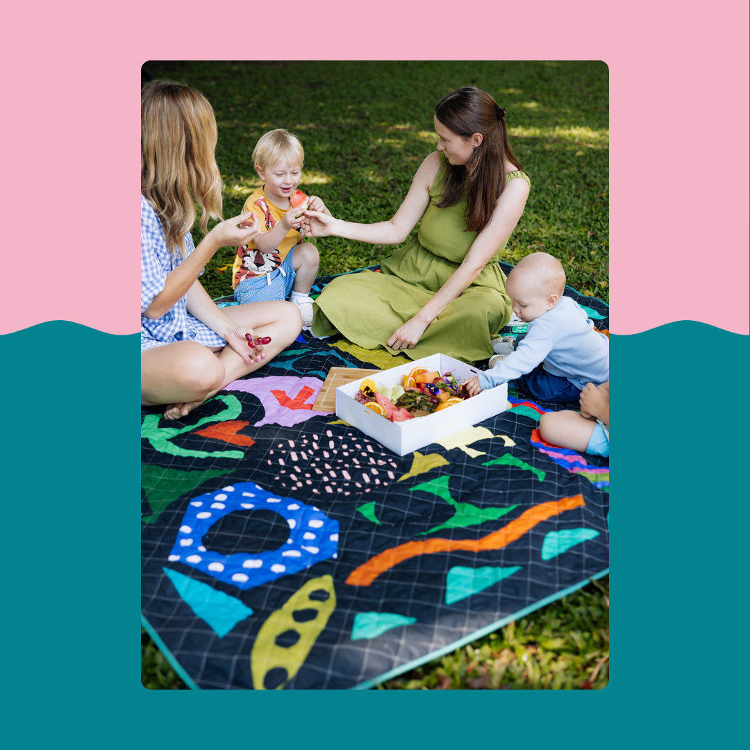 family picnic on dark patterned rudie nudie jumbo picnic rug on grass with kids and food