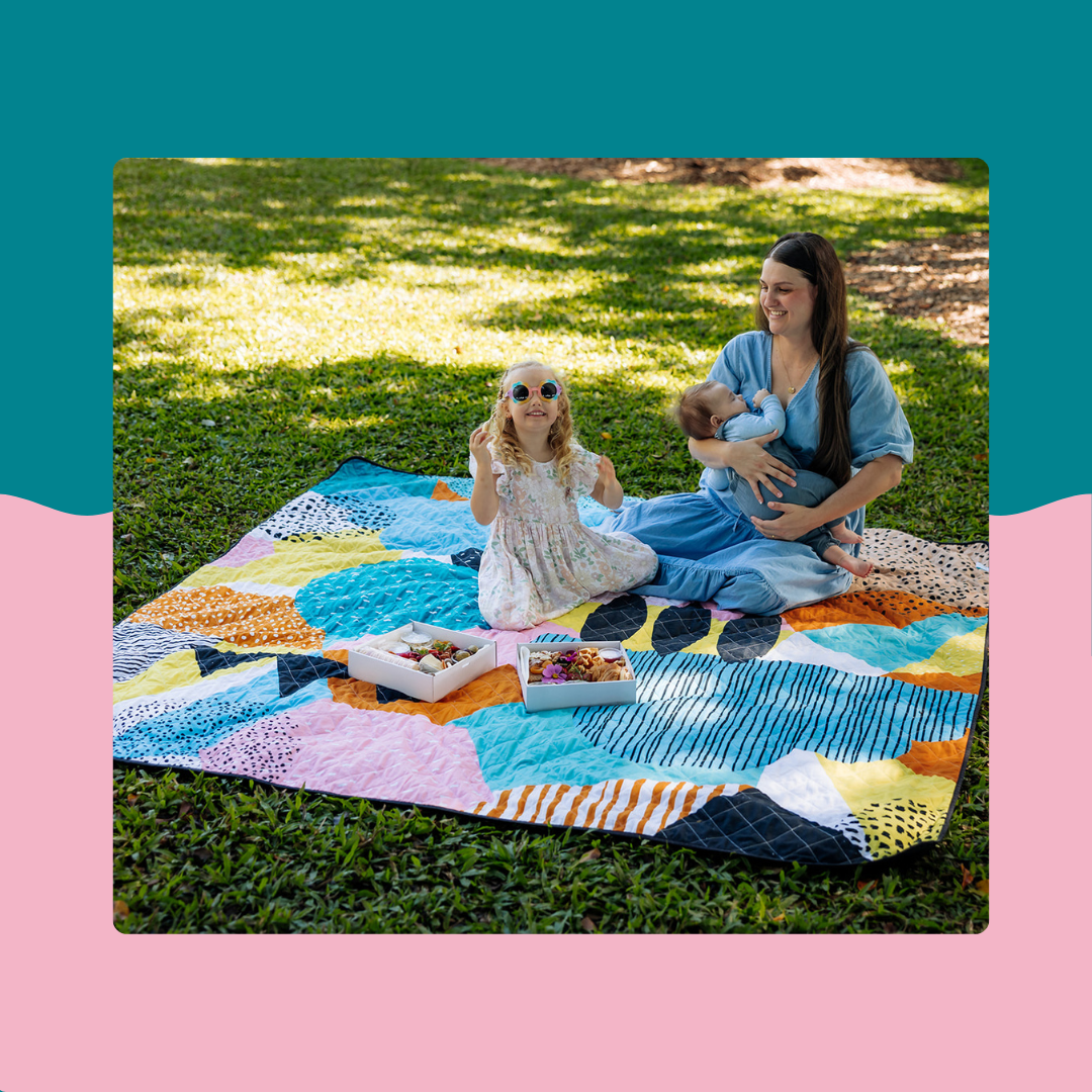 mum and children relaxing on colourful rudie nudie jumbo picnic rug on grass with snacks