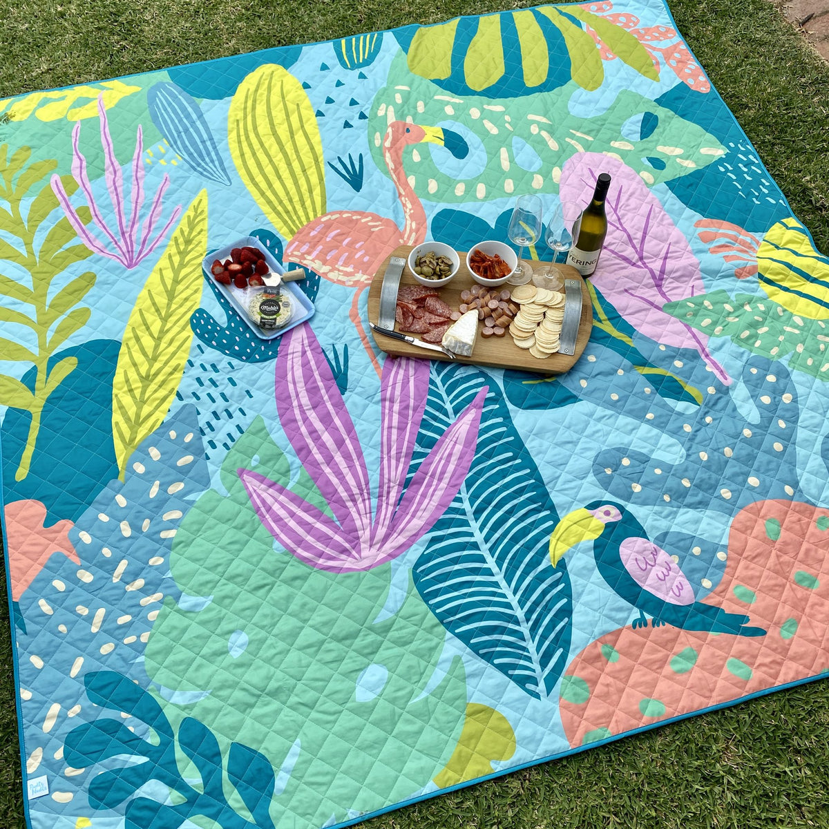 flamingo-a-go-go waterproof picnic blanket laid out on the lawn with a grazing platter