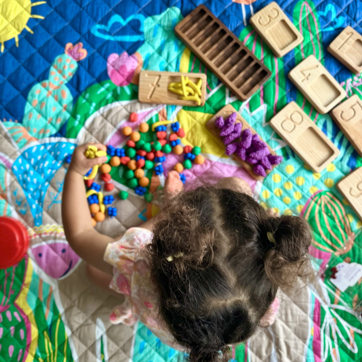 overhead view of a child doing counting play on the hola mamacita large waterproof playmat