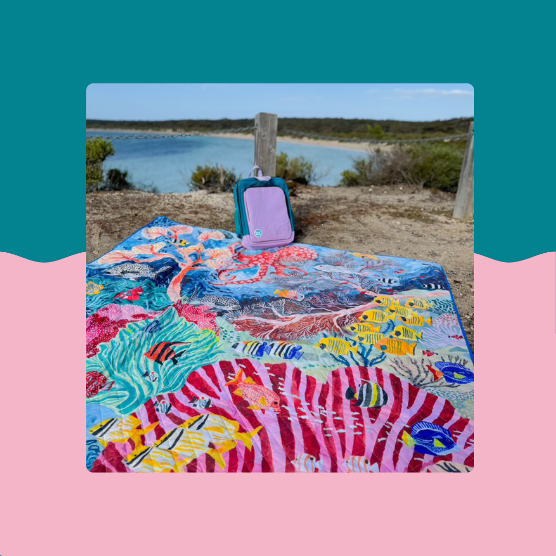 colourful big day out jumbo picnic rug spread on grass by the water with a backpack and hat