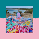 colourful big day out jumbo picnic rug spread on grass by the water with a backpack and hat