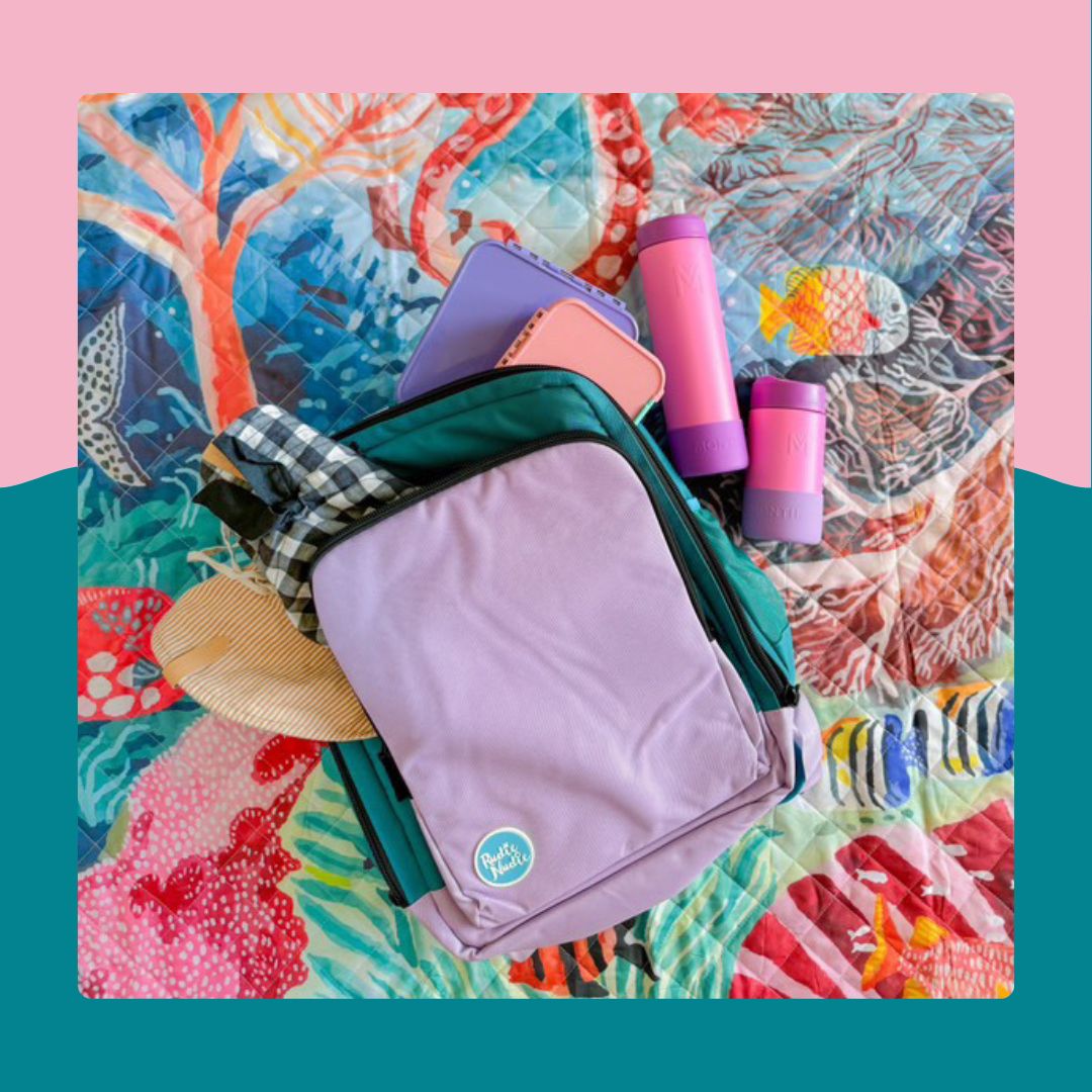 lilac on teal rudie nudie nappy backpack with bottles and hat on colourful reef-print playmat