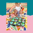 baby on colourful rudie nudie play mat playing with muffin tin during nappy free time