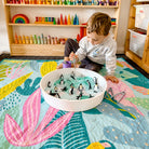 toddler playing with a sensory tray on the flamingo-a-go-go large waterproof playmat