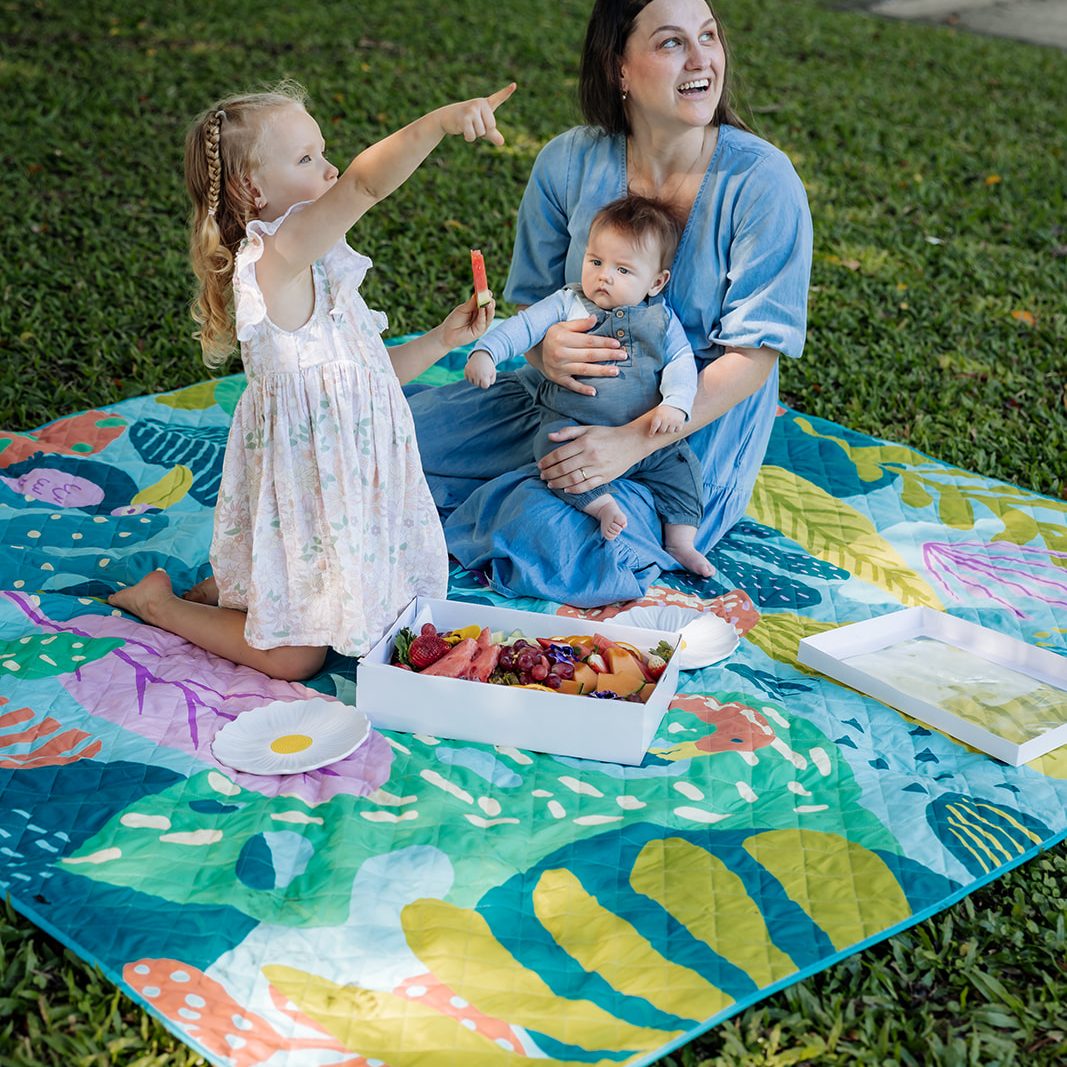 mother with baby and daughter having a picnic on the flamingo-a-go-go waterproof picnic blanket