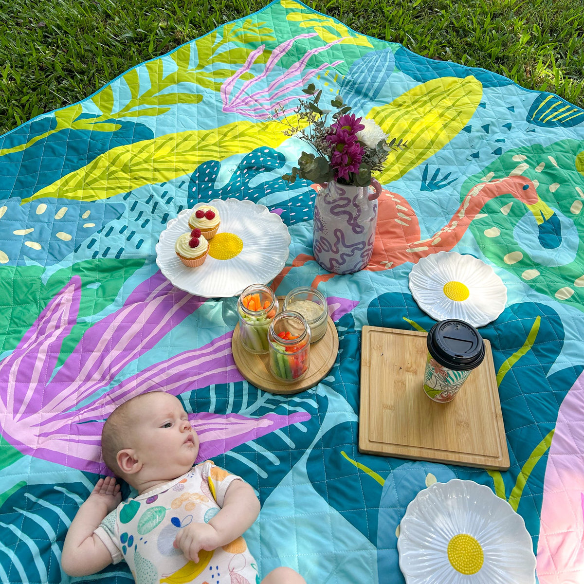 baby lying on the flamingo-a-go-go waterproof picnic blanket set for a picnic in the garden