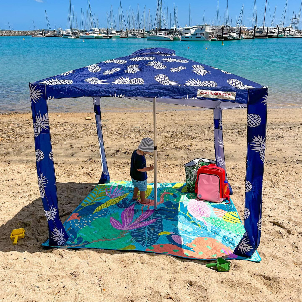 child under a beach cabana on the flamingo-a-go-go picnic blanket with umbrella hole by a marina