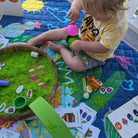 toddler doing sensory rice play on the hola mamacita large waterproof playmat