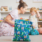 mother packing a hola mamacita wet bag in a playroom with her children