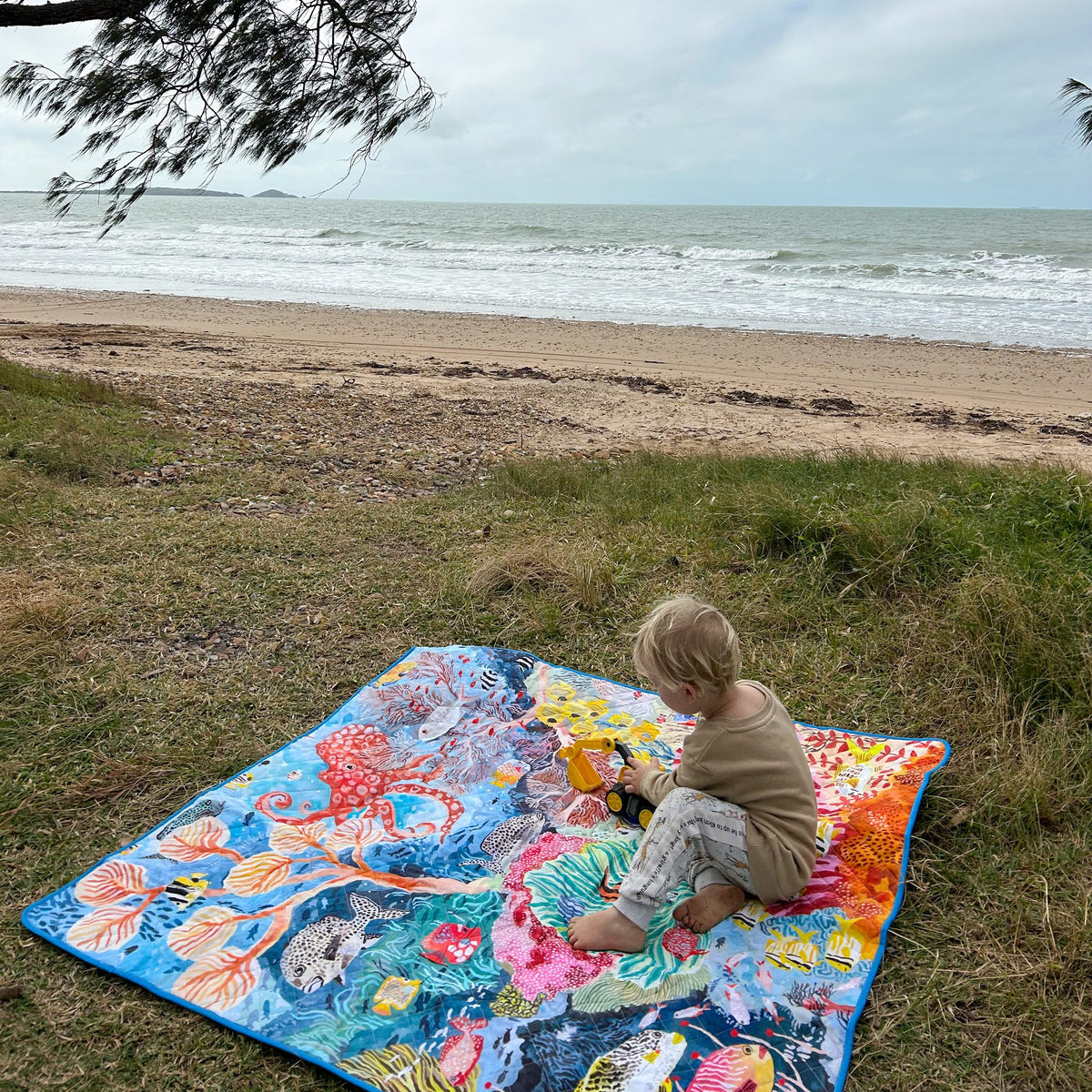 toddler playing on the octopus's garden large waterproof playmat on grass by the beach