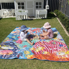 two children playing on the octopus's garden waterproof picnic blanket in front of a playhouse