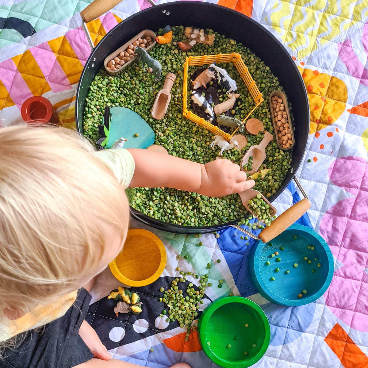 overhead view of a toddler playing with a sensory tray on the pop pip pow large waterproof playmat