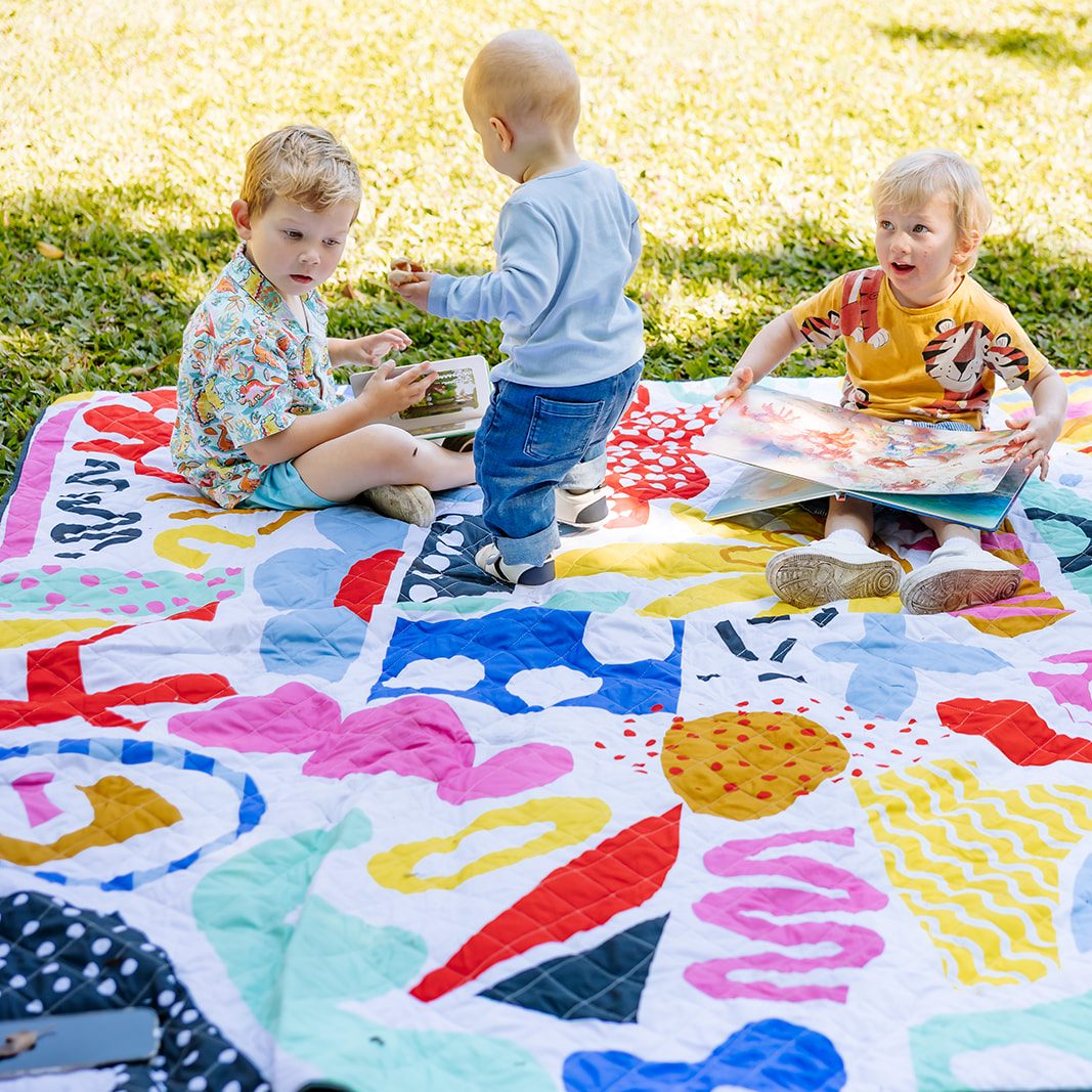 three toddlers playing on the pop pip pow waterproof picnic blanket in the park