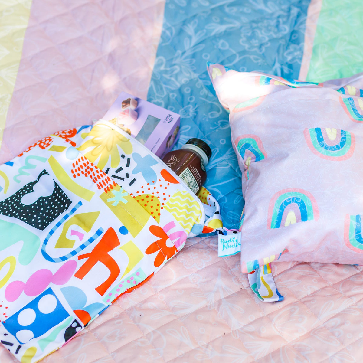 pop pip pow wet bag packed with essentials beside a rainbow wet bag