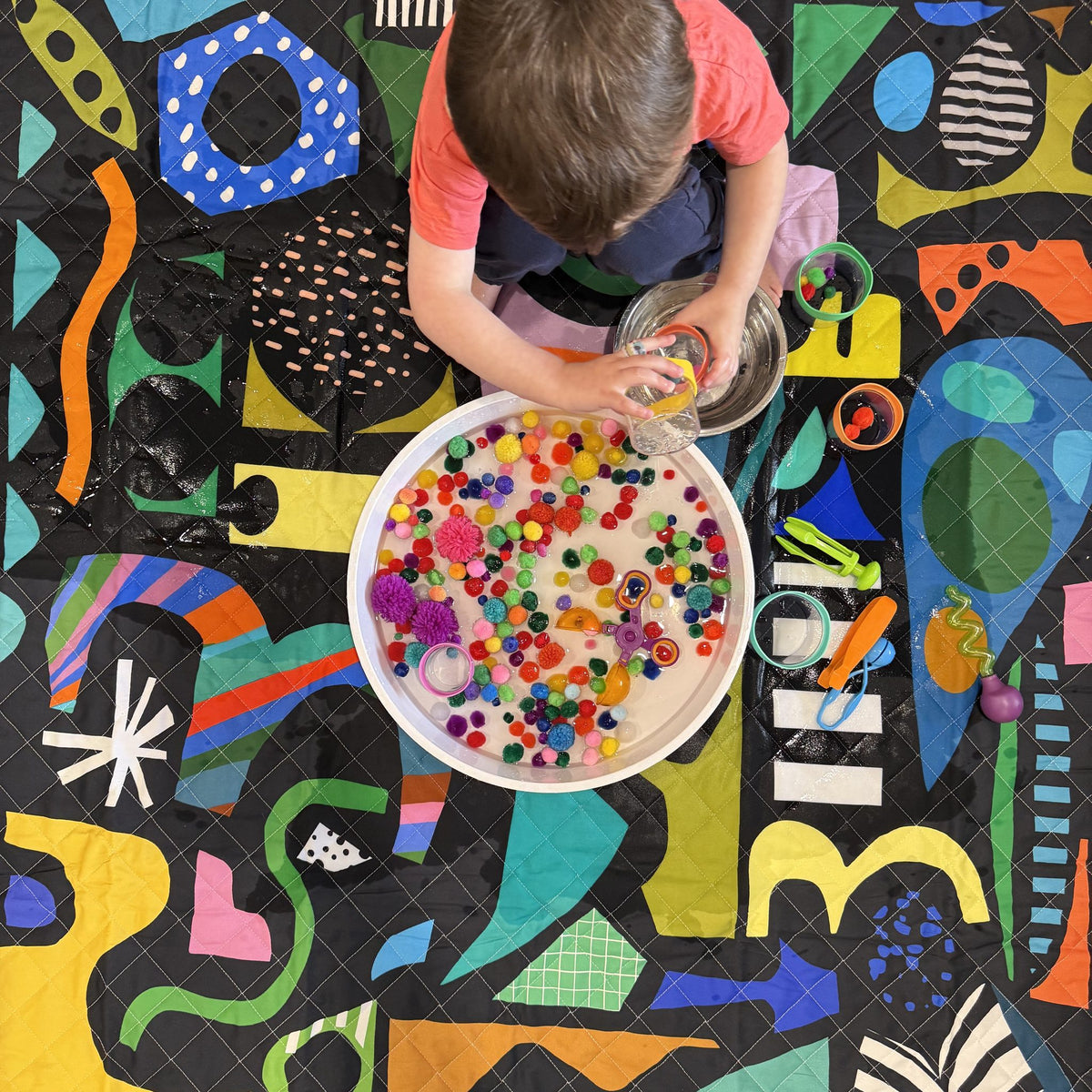 overhead view of a child doing pom pom sensory play on the rock candy large waterproof playmat