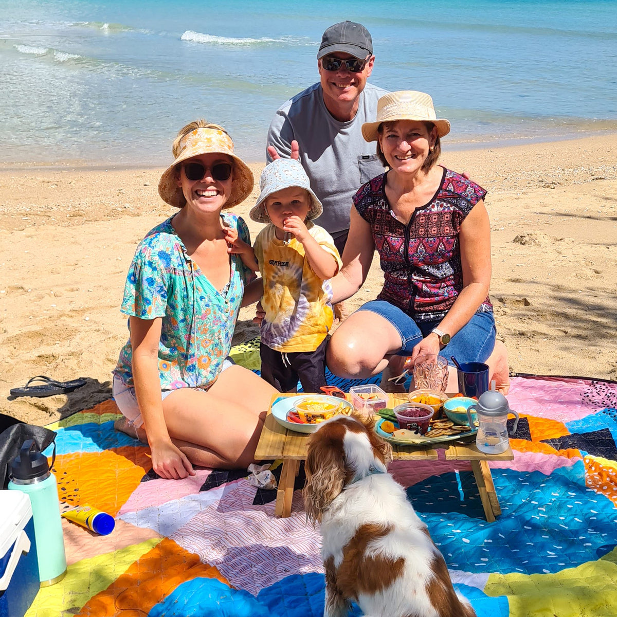 family with a toddler and dog on the happy now waterproof picnic blanket at the beach