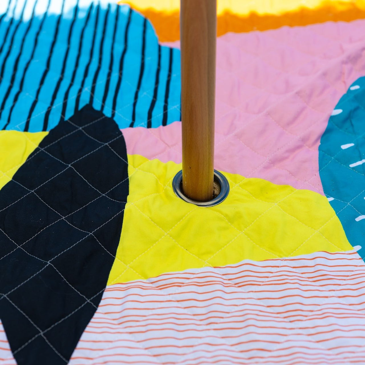 close-up of a timber umbrella pole through the middle of the happy now picnic blanket with umbrella hole